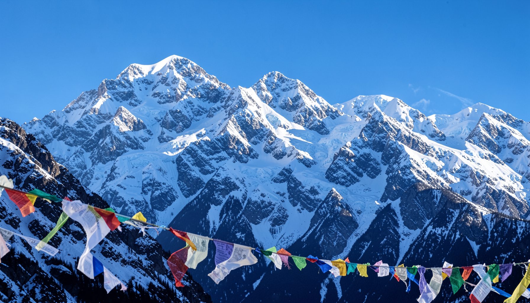 Snow-dusted mountain peaks under a crisp blue sky, with prayer flags fluttering in the foreground, cool whites and deep blues